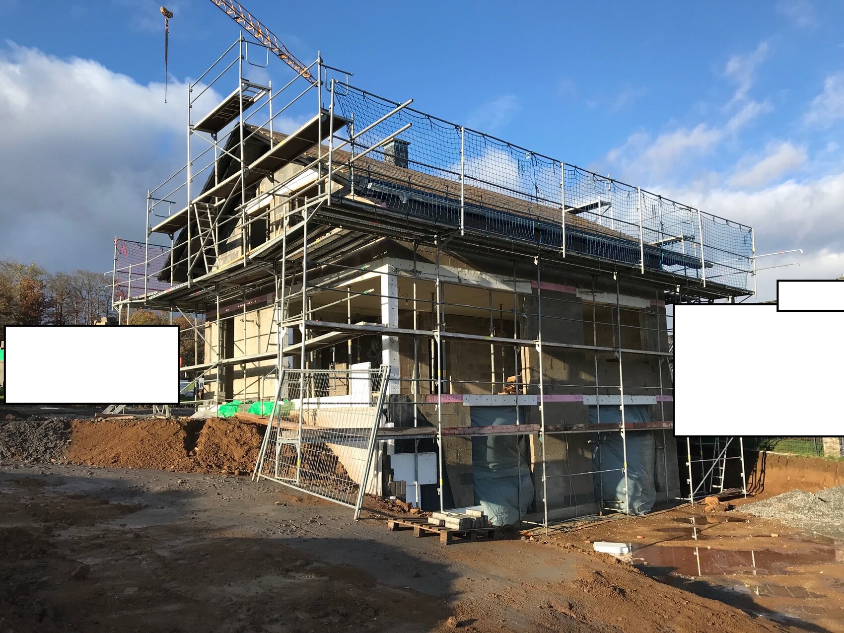 Construction site with scaffolding around the building; crane in the sky, mud and materials.