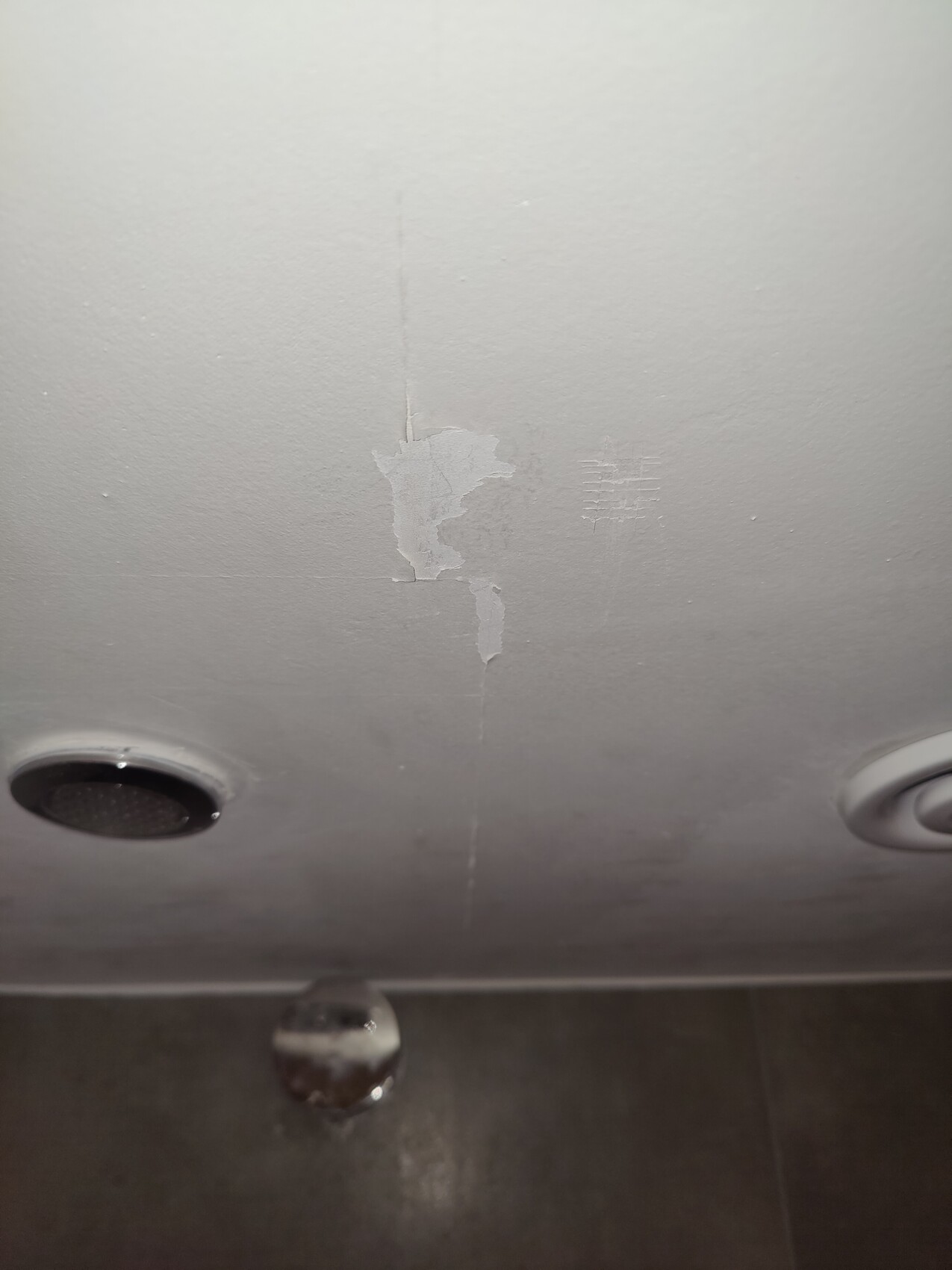 Wall/ceiling with peeling paint and cracks; two round covers at the bottom, dark floor.
