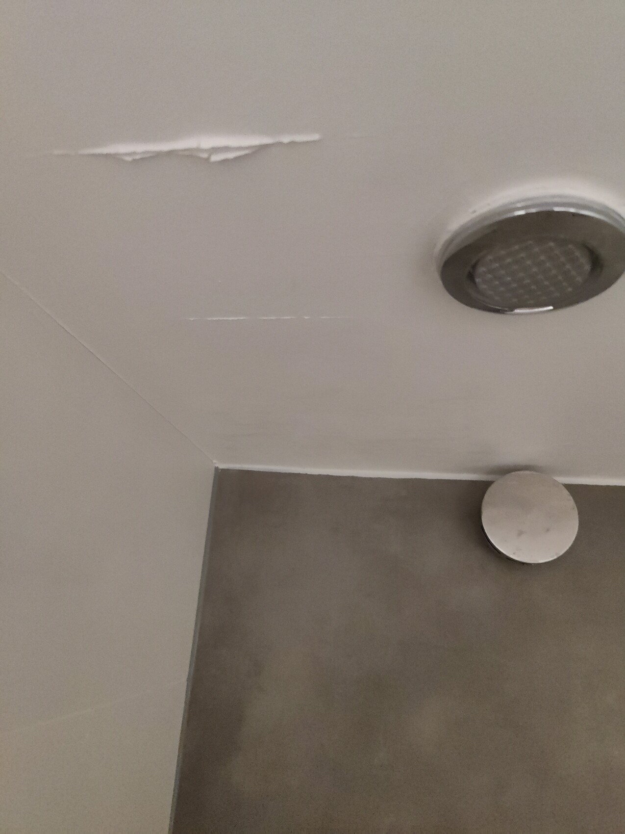 Bathroom ceiling with spalling, round showerhead on the ceiling, gray wall below.