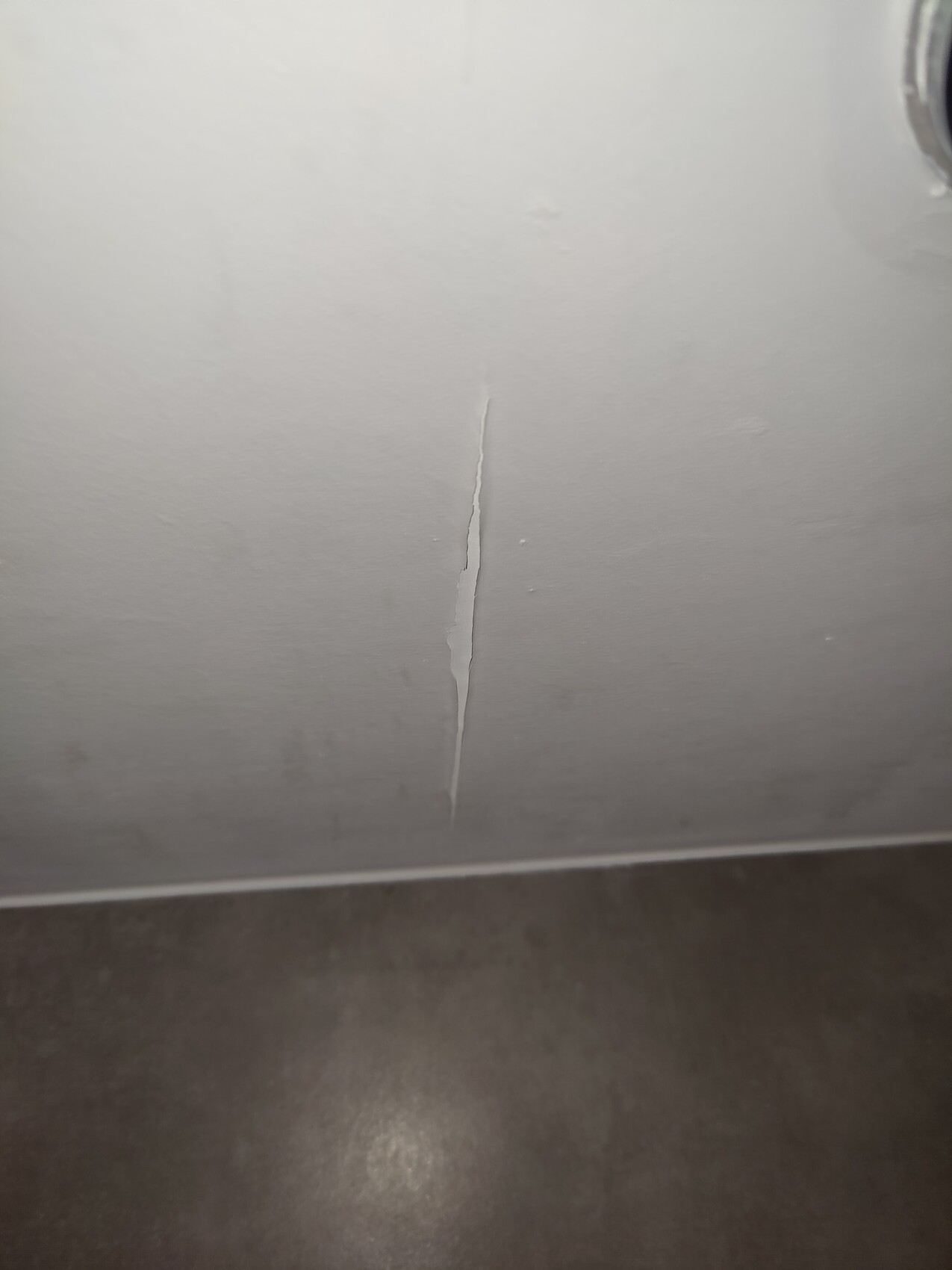 Light-colored wall with vertical crack from top to bottom, dark floor below.