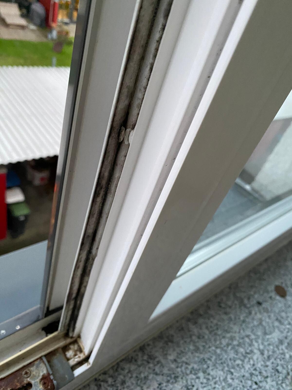 Close-up of a white window frame with dirty rubber seal and rust at the bottom edge.