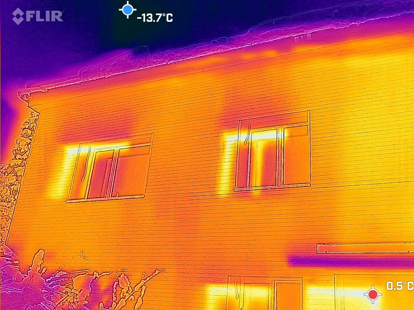 Thermographic image of a multi-story house at night; warm window frames, cold exterior wall.