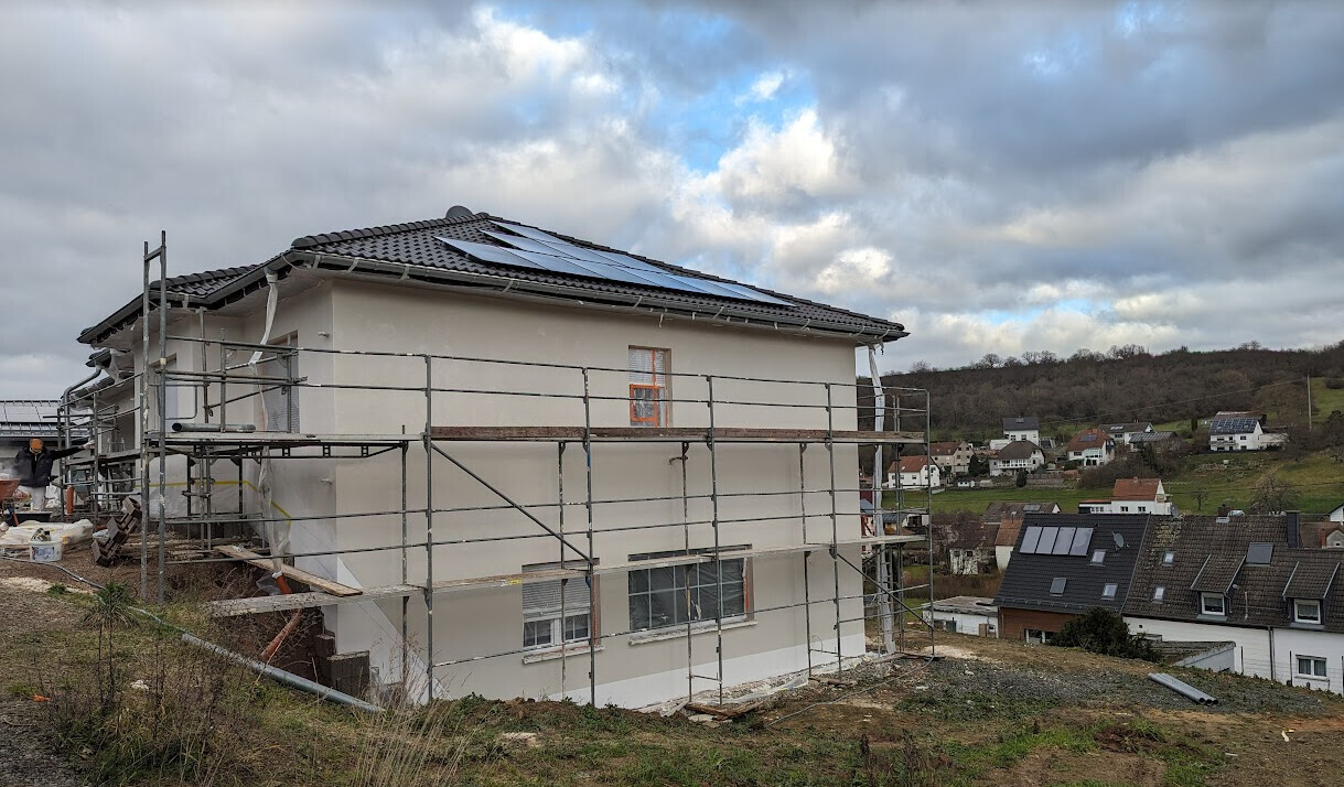 House in shell construction with scaffolding and solar panels on the roof.