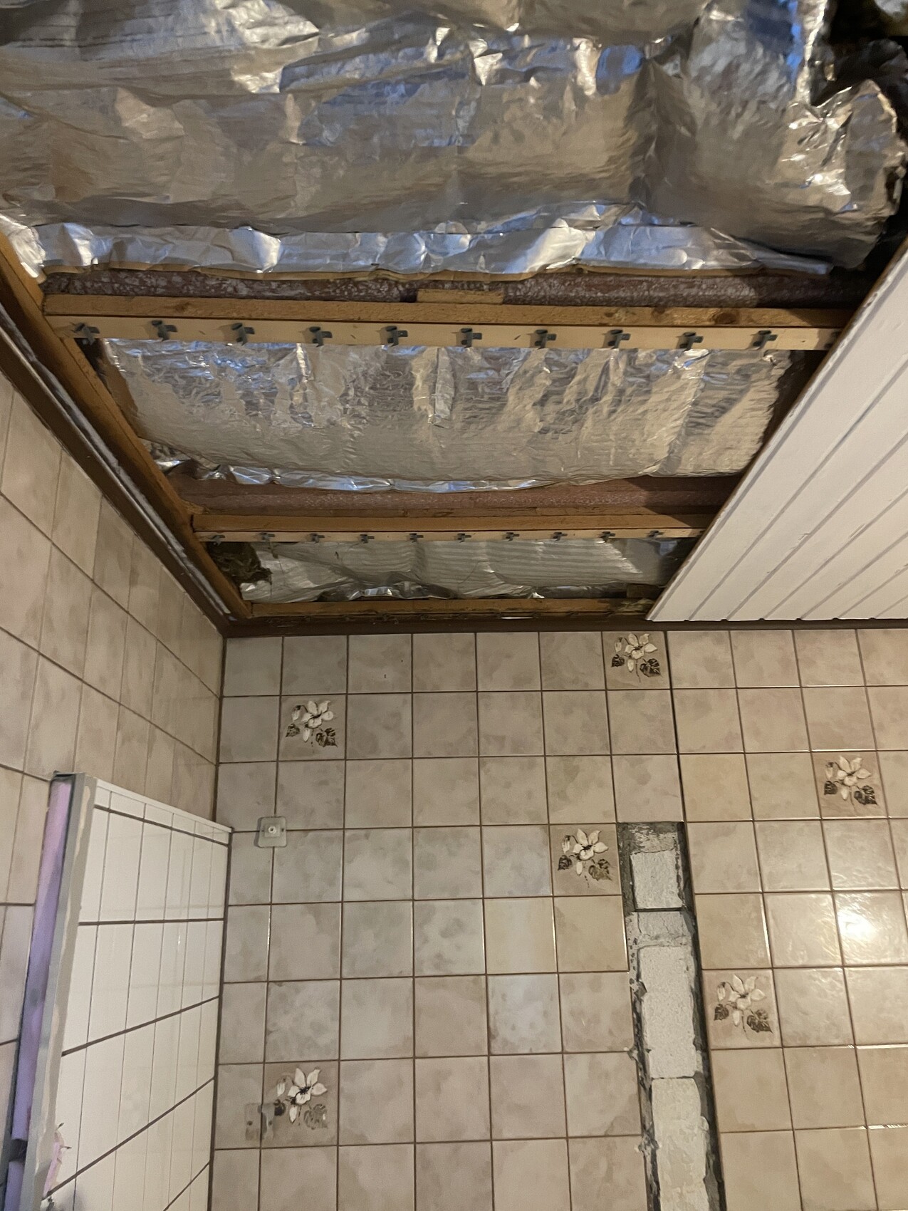 Bathroom under construction: open ceiling with insulation, foil, and tiled floor.