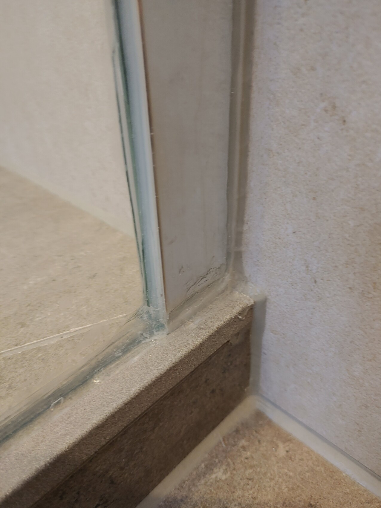 Close-up of a shower door glass frame in the bathroom with silicone sealant and tiles