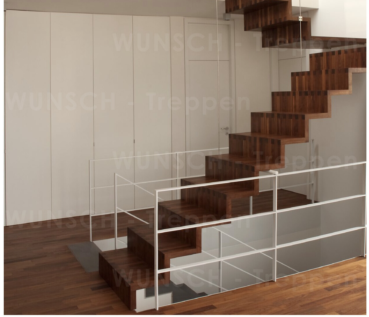 Modern indoor staircase made of dark wood with cantilevered steps and white railing.