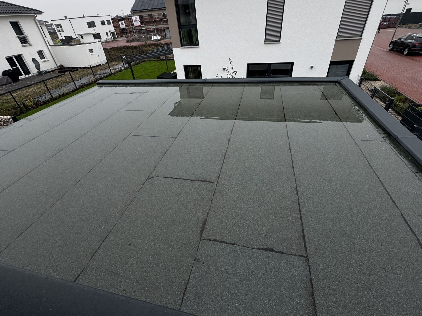 Top view of flat roof with puddle; behind it a modern white house.