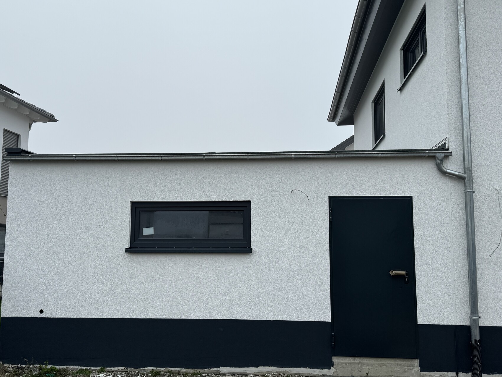 Exterior view of a white building with dark door, narrow window and visible gutter