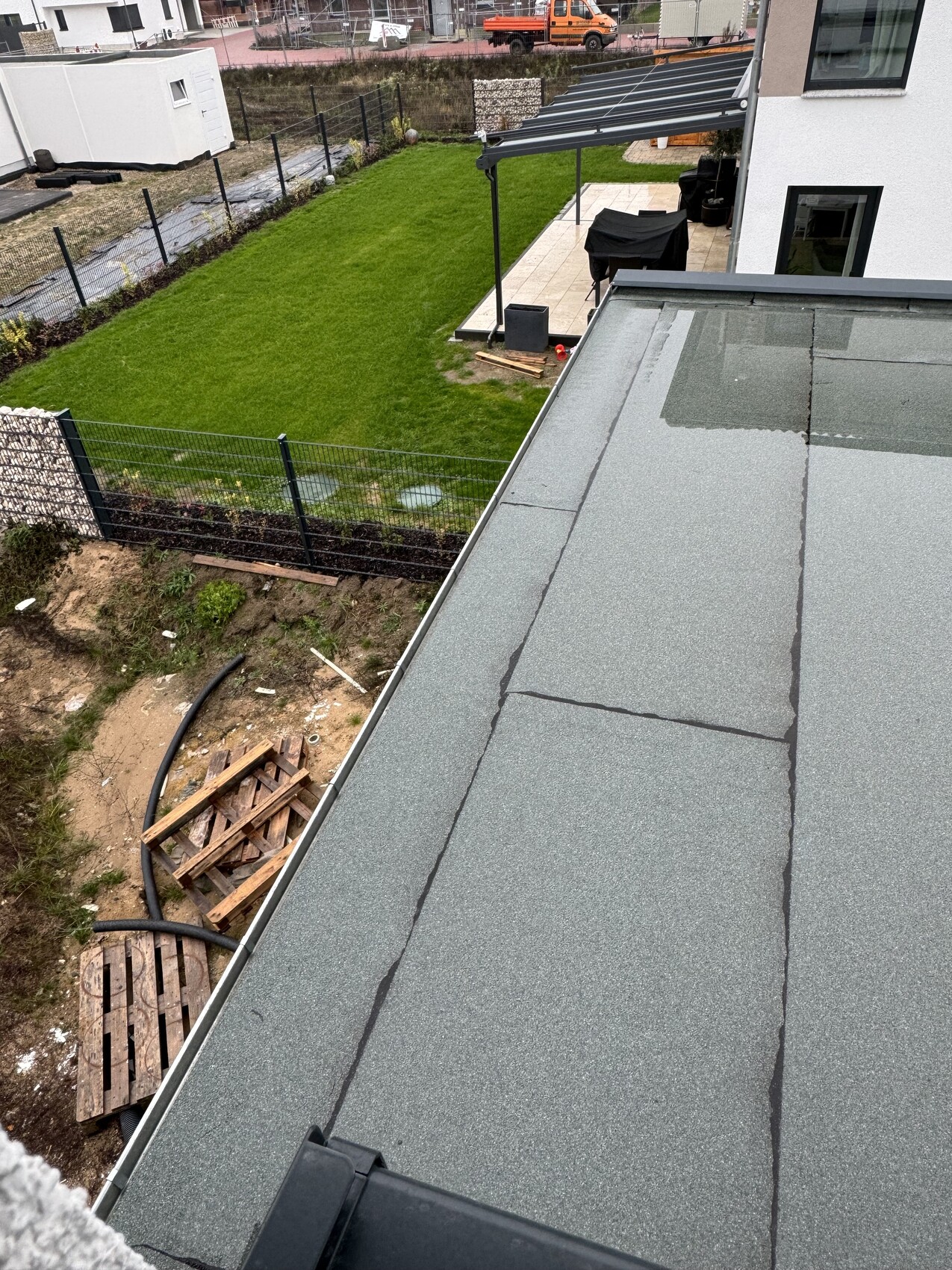 View from roof onto green garden area, terrace with grill under pergola and construction work in the background