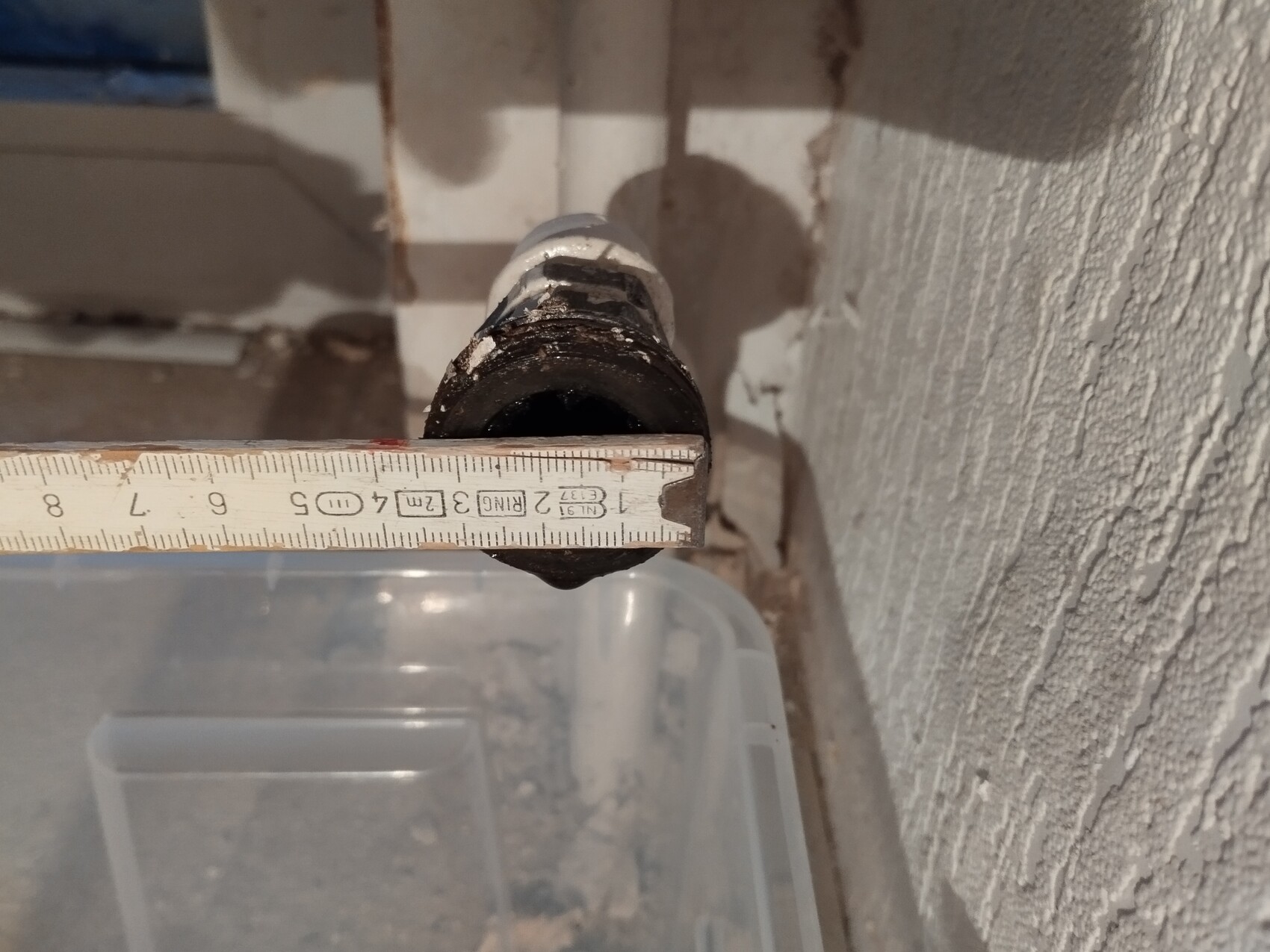 Close-up of a pipe with a measuring tape measuring the hole diameter, wall in the background