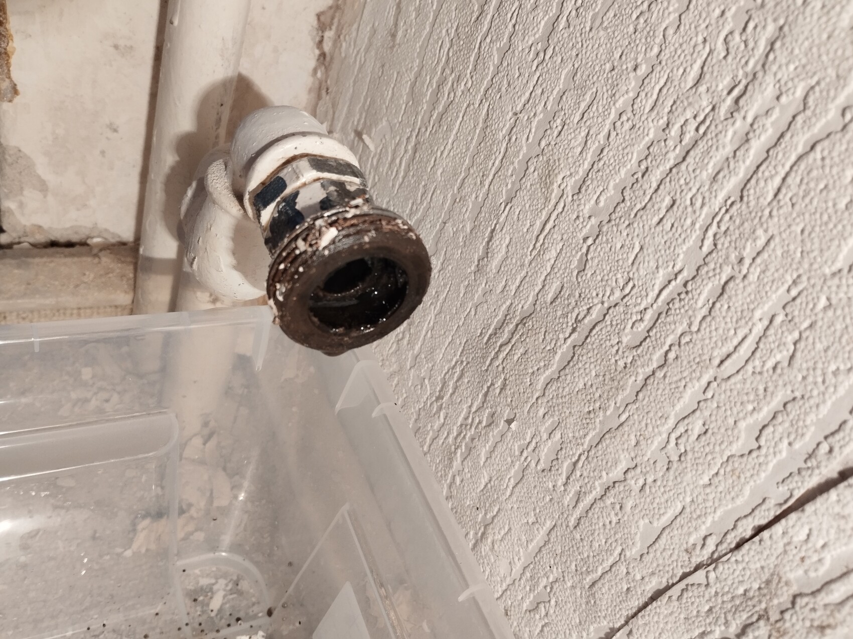 Rusty pipe end with dark interior surface, on a rough white wall.
