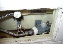 Pipework behind wall with metal valve and connections visible.