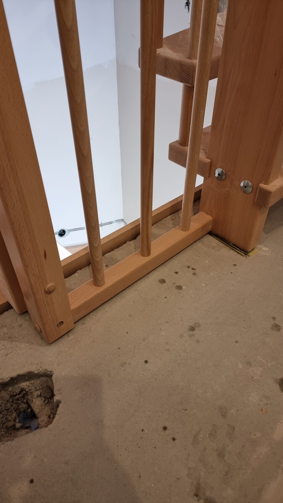 Wooden staircase with railing posts, construction progress, concrete floor with hole on the lower left.