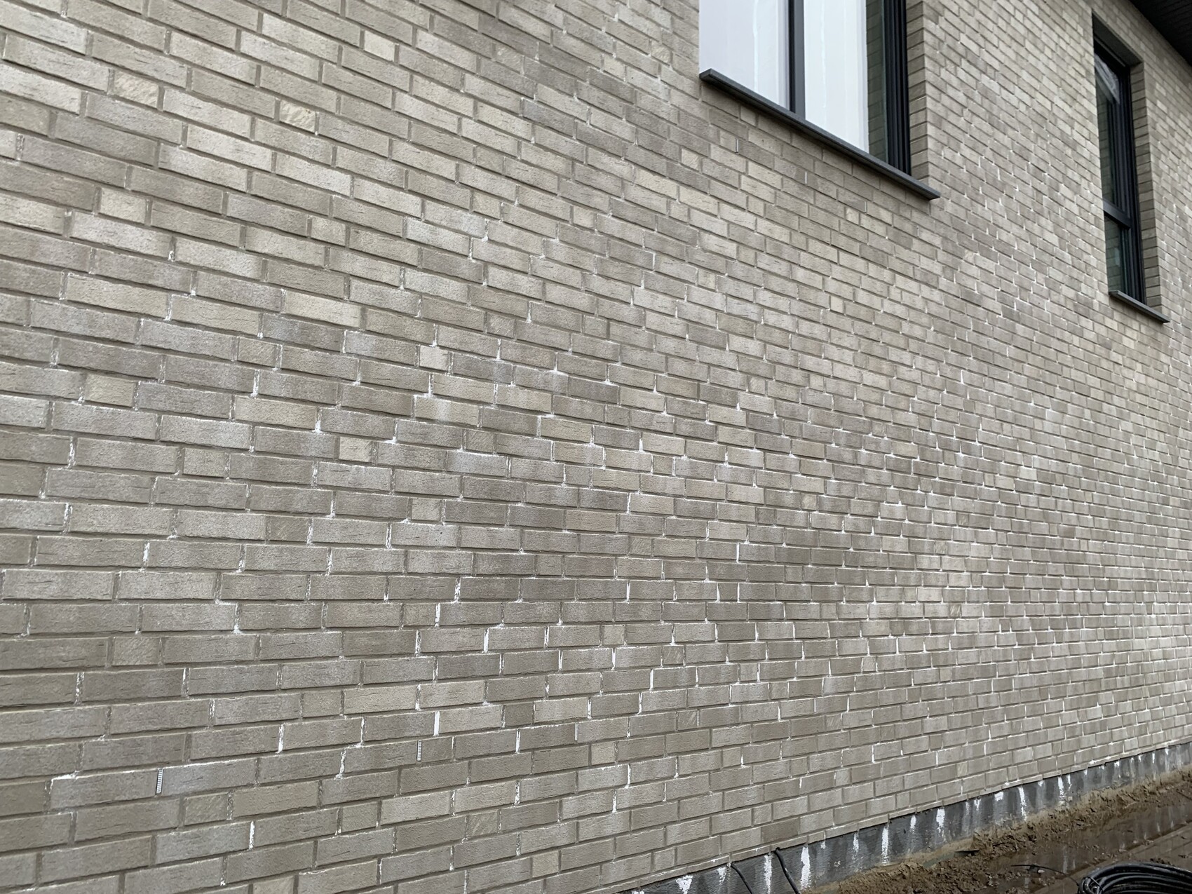 Beige brick wall of a building with two windows at the top right; foundation floor visible