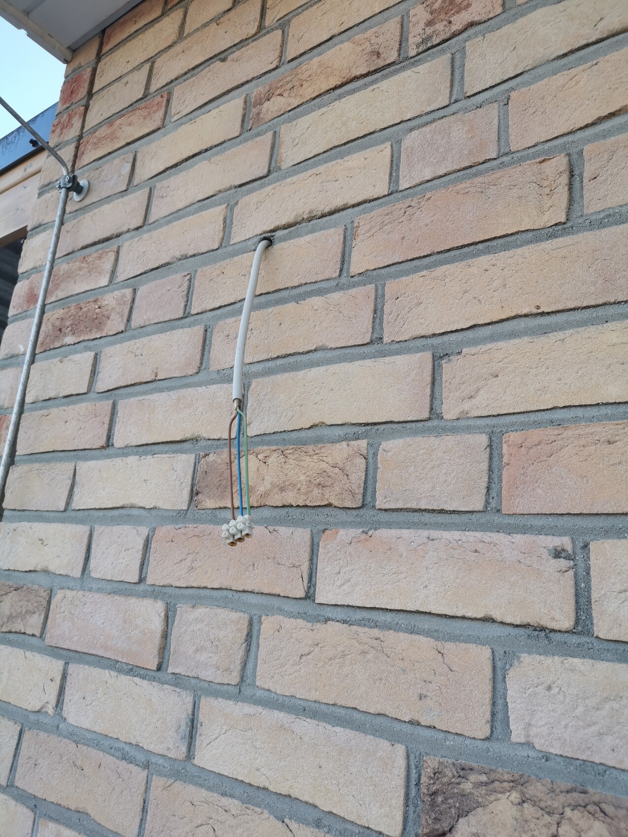 Exterior wall made of bricks; white cable conduit hanging vertically ending in a connector.