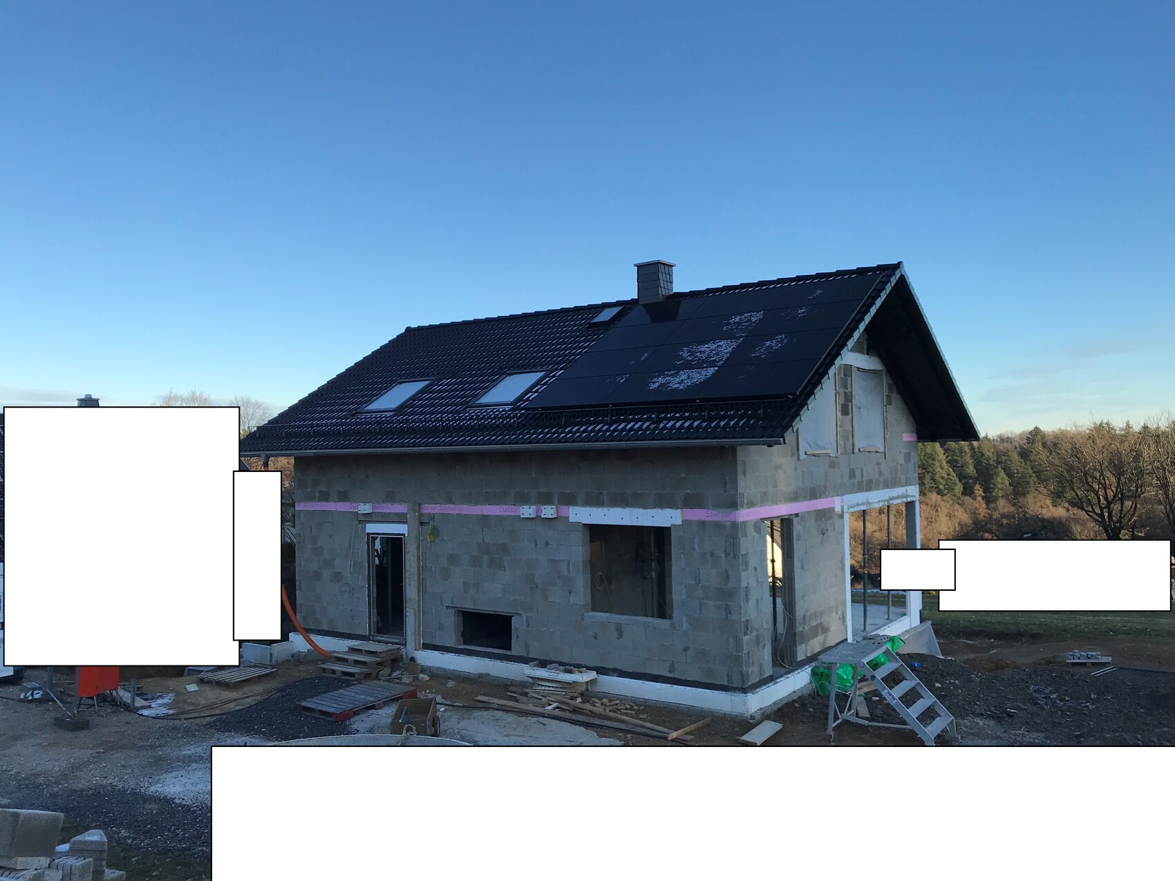New house construction: shell made of concrete blocks, dark roof with solar panels, construction equipment outside.