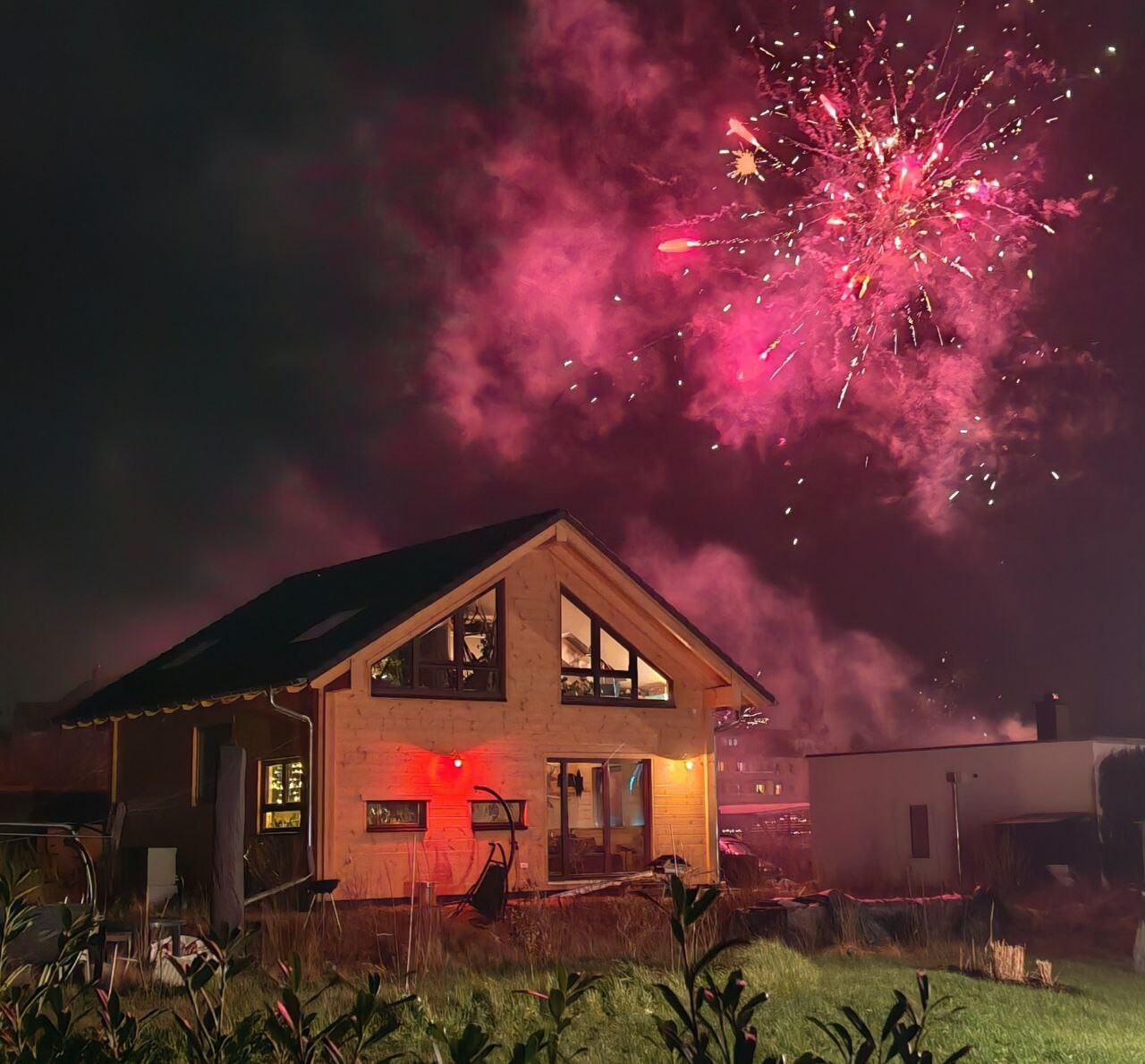 Modern house at night with pink fireworks in the sky above the garden.