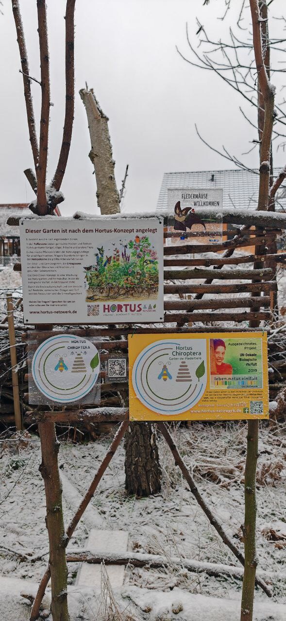 Winter garden entrance made of branches with posters about the Hortus concept, snow.