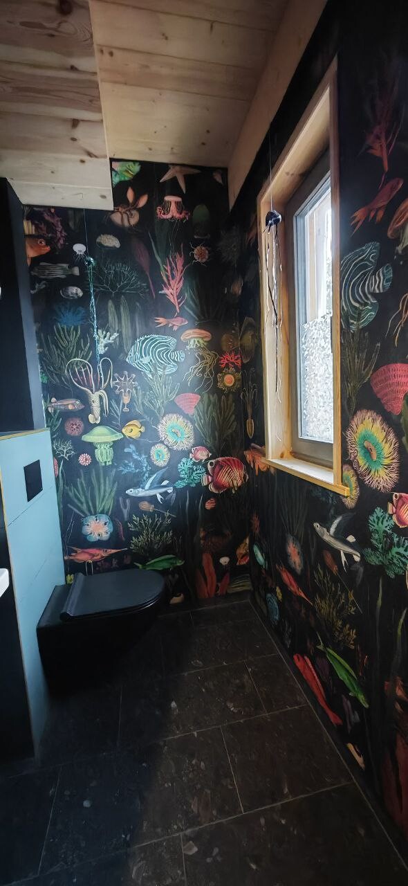 Bathroom with colorful underwater wall decal, window, toilet, and dark tiles.
