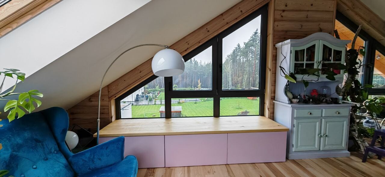 Attic with large triangular window, blue armchair, plant cabinet, and garden view.