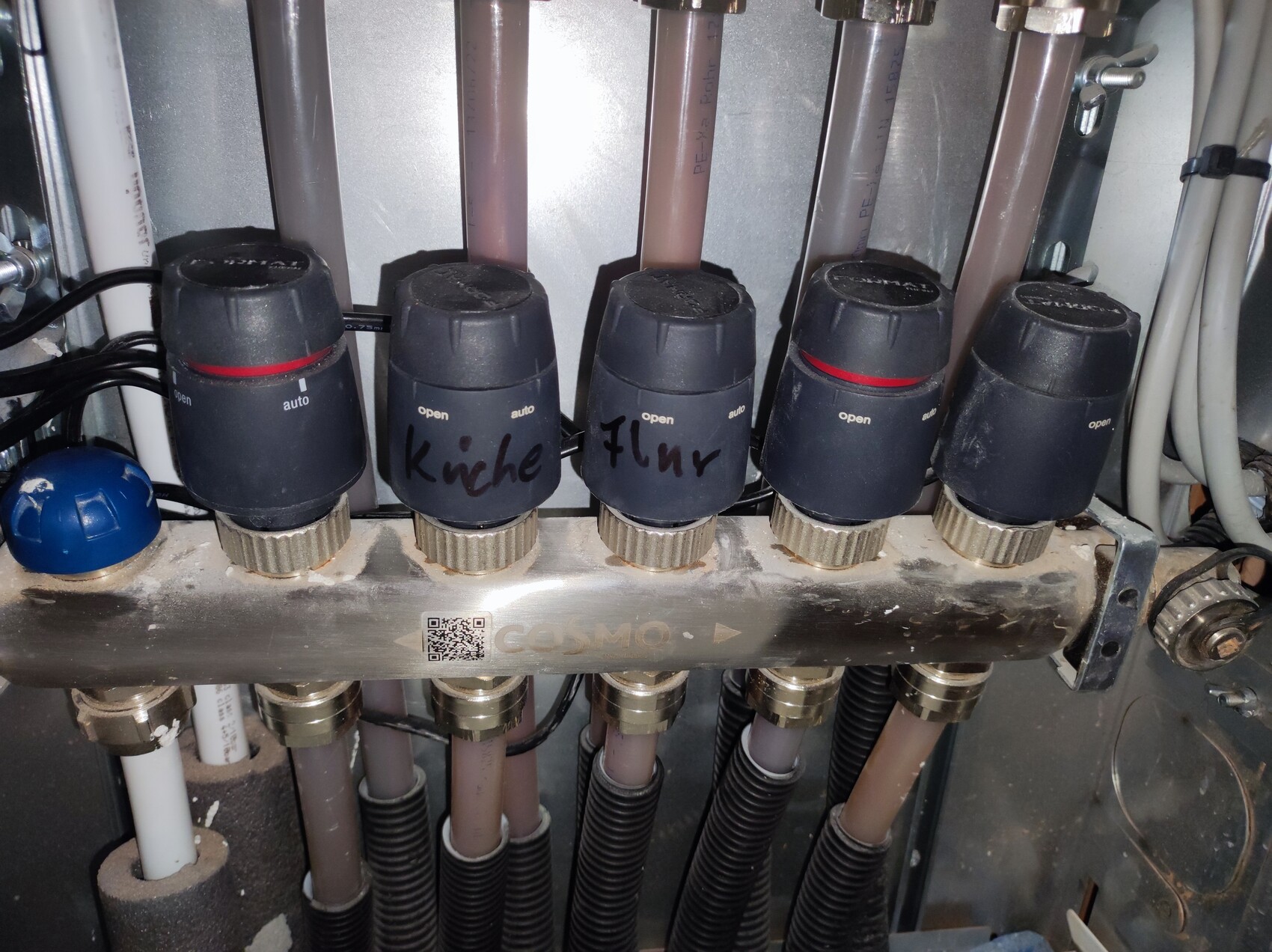 Five black rotary knobs with red rings on a metal block, hoses behind.