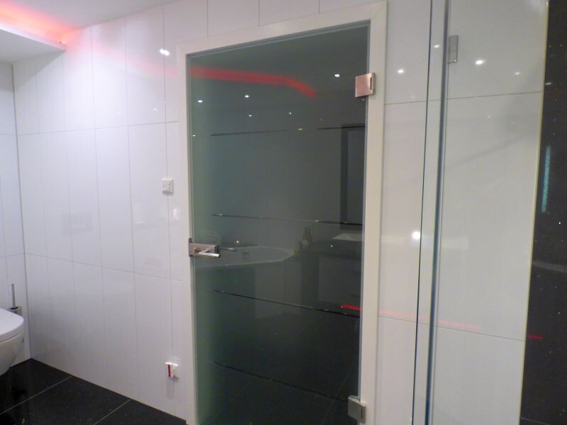 Moderne Badezimmeransicht mit Glas-Tür, weißen Fliesen, linkem Waschbecken und rotem Lichtband.