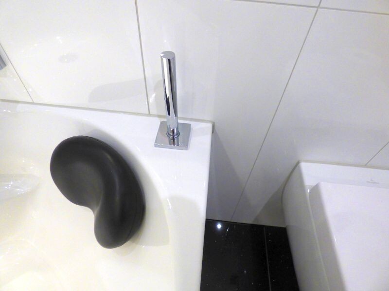 Badezimmer: weiße Badewanne mit schwarzem Nackenkissen und Armatur, Toilette daneben.