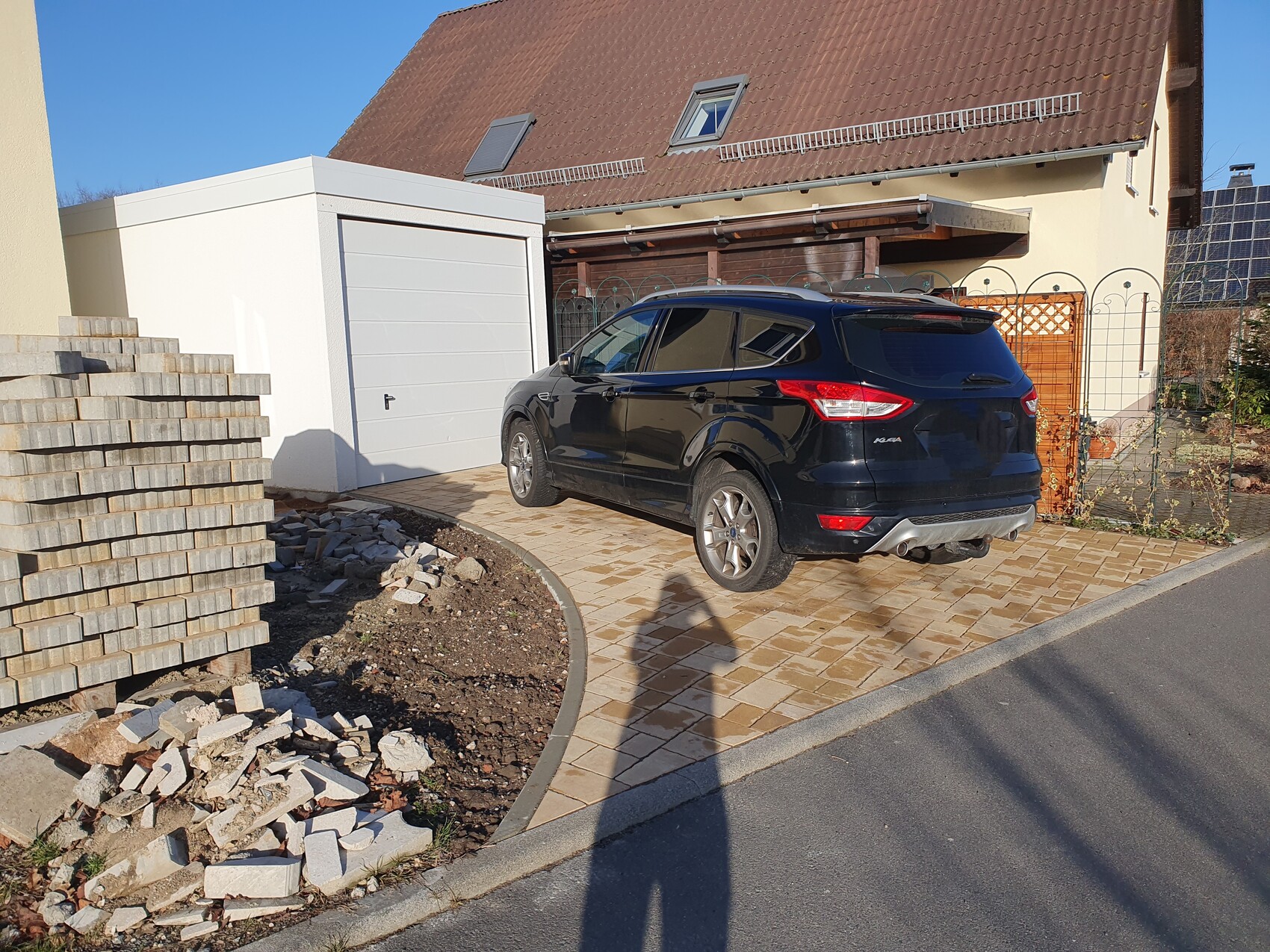 Black SUV in paved driveway in front of white garage; construction debris on the left.