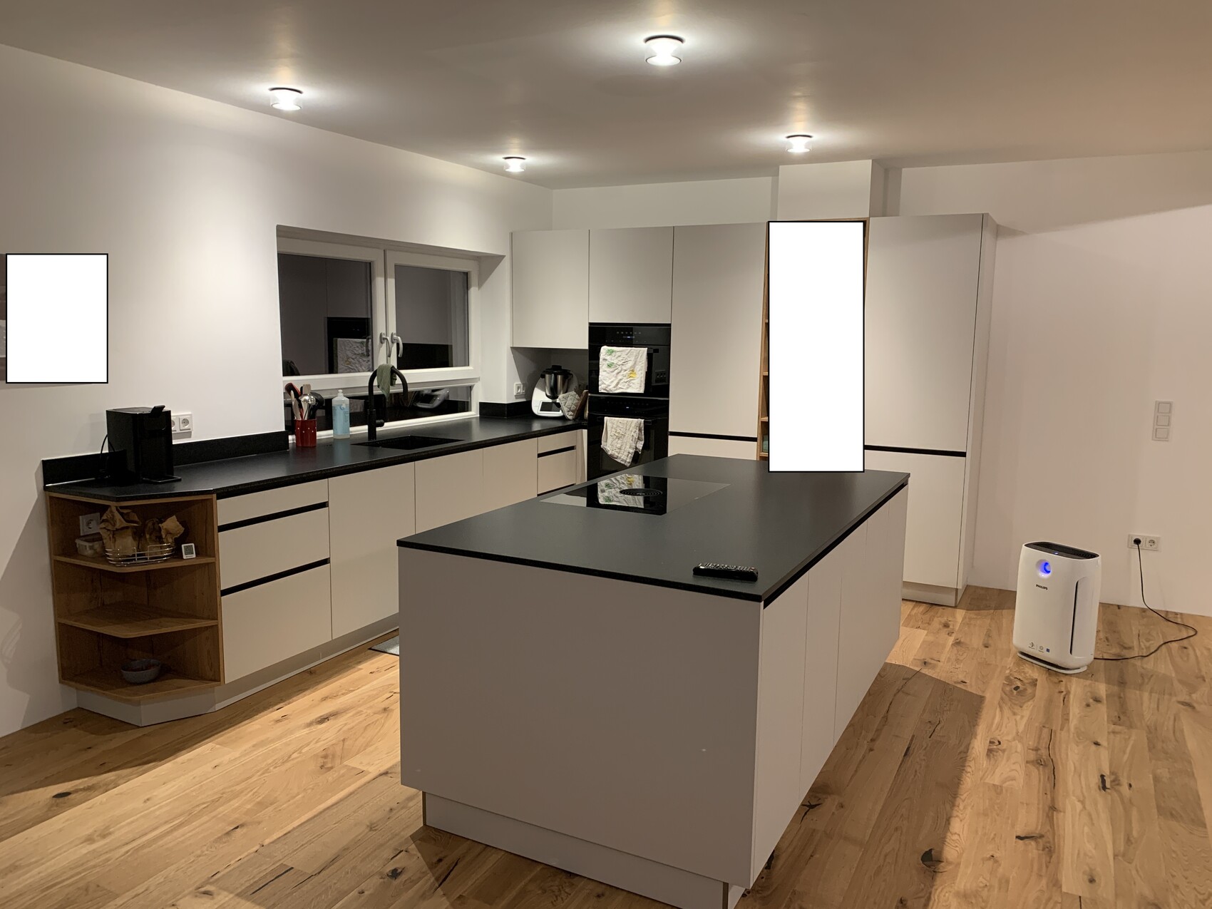 Moderne Küche mit zentraler Insel, weißen Schränken, schwarzen Arbeitsplatten und Holzboden.