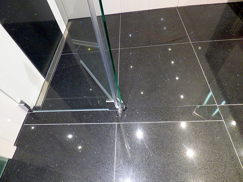 Modern glass shower enclosure in a bathroom with black glossy floor tiles.