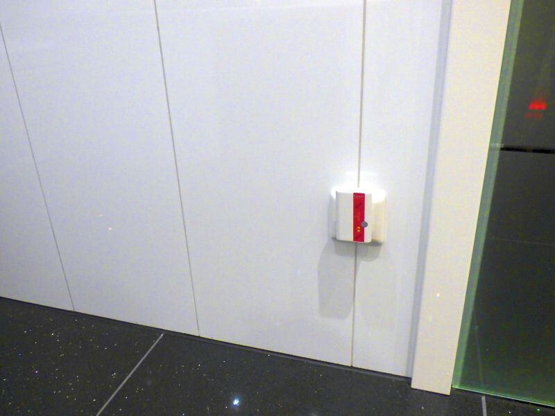 White wall panels with small white light switch and red stripe, dark floor, glass side.