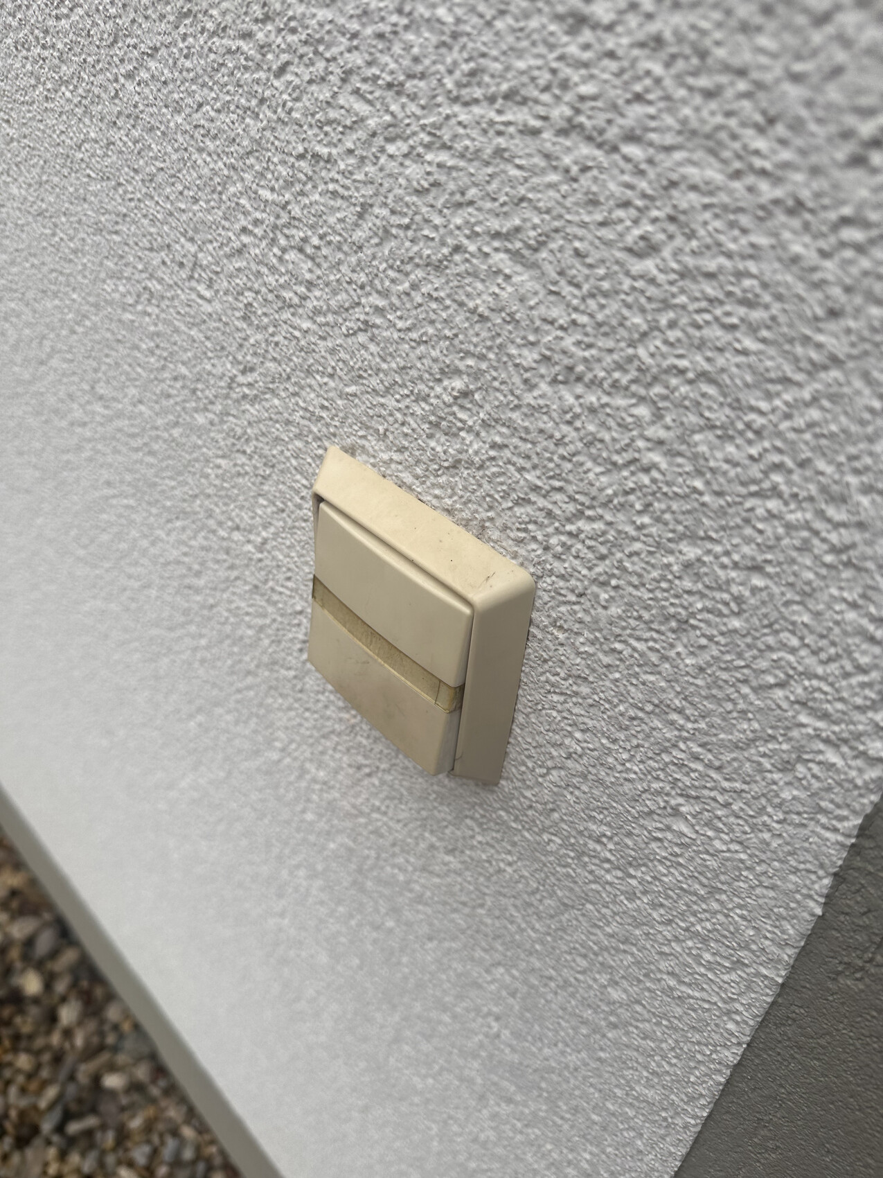 Beige double light switch on rough plaster wall, slightly dirty