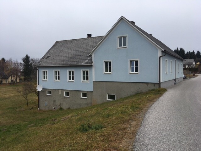 Exterior view of a blue house on a hillside next to a road