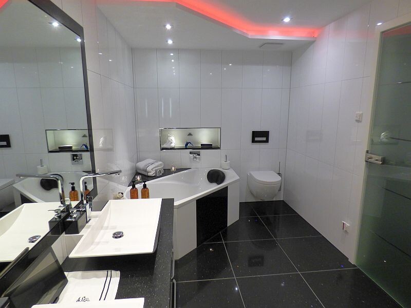 Modern bathroom with corner bathtub, sink, toilet, mirror, and glass shower.