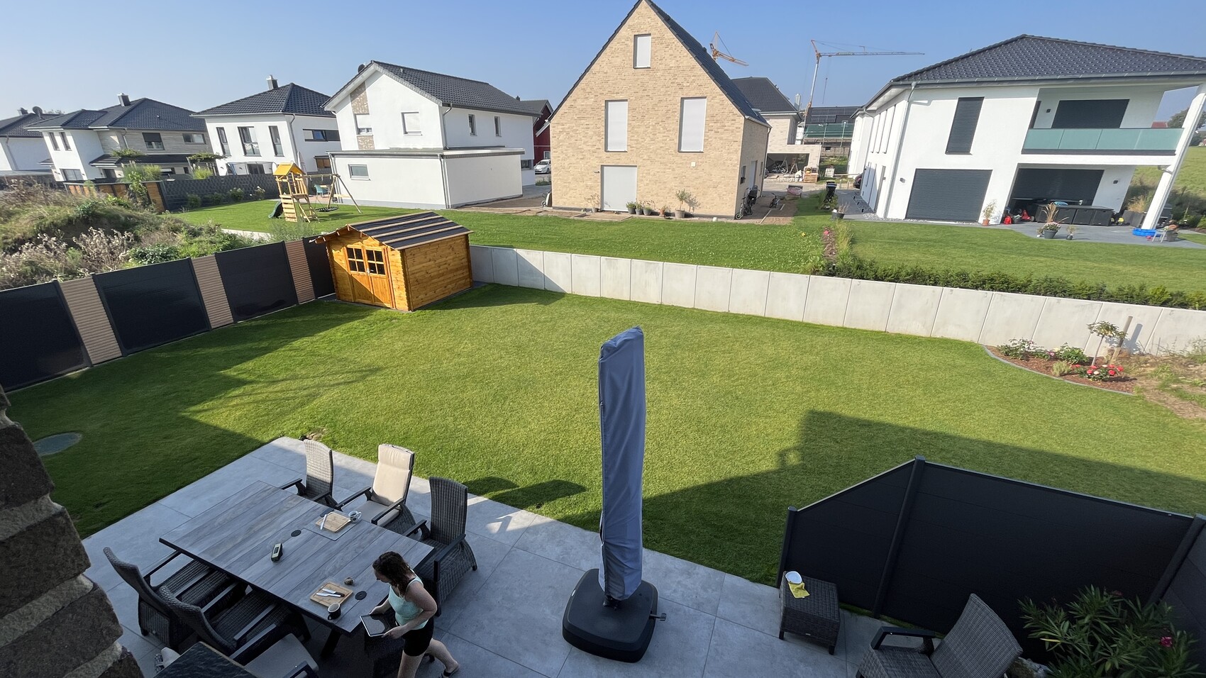 Backyard with green lawn, wooden garden shed, play equipment, and dining table on the terrace.