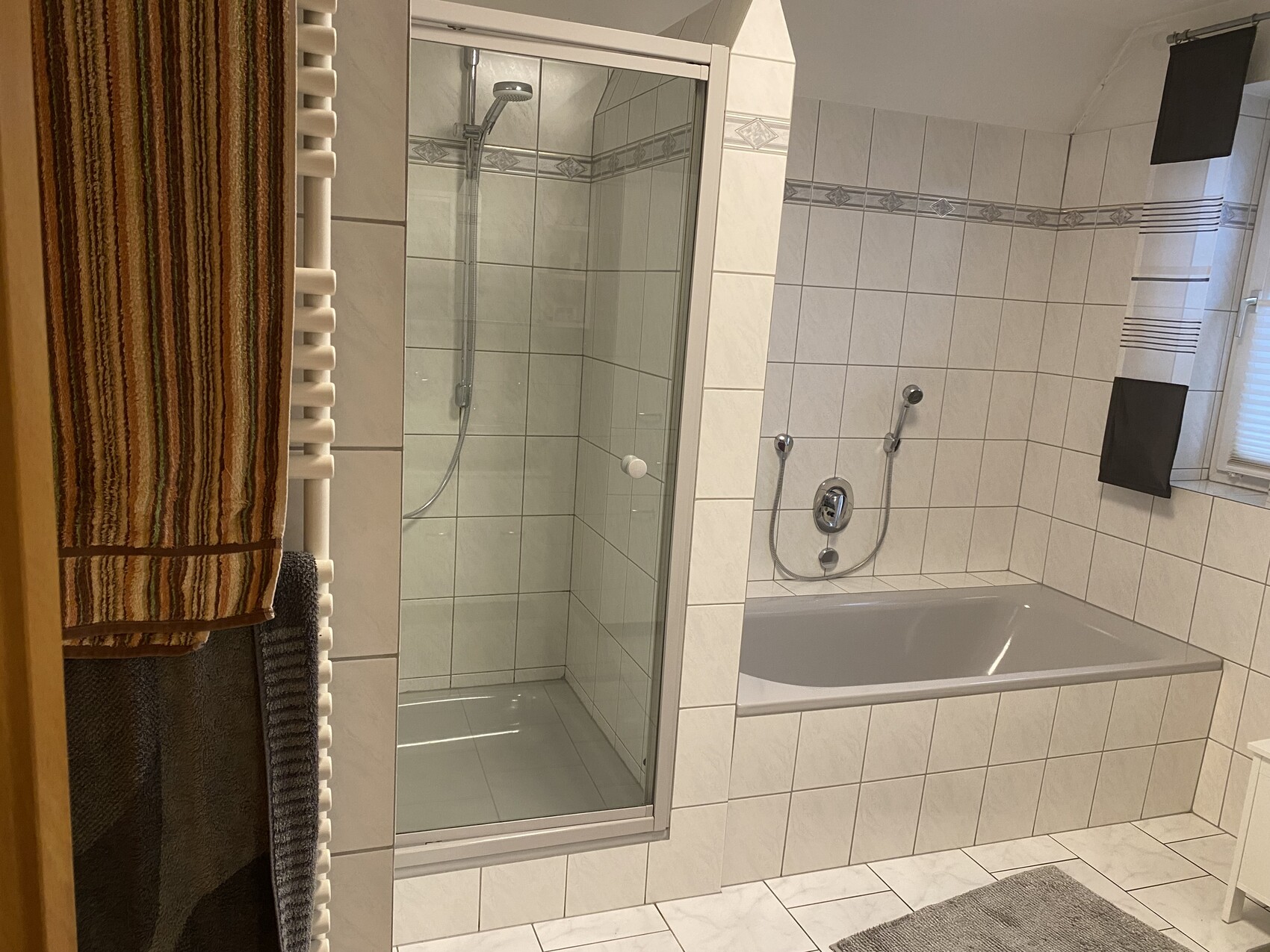 Bathroom with glass shower, bathtub and radiator with orange-striped and gray towels.