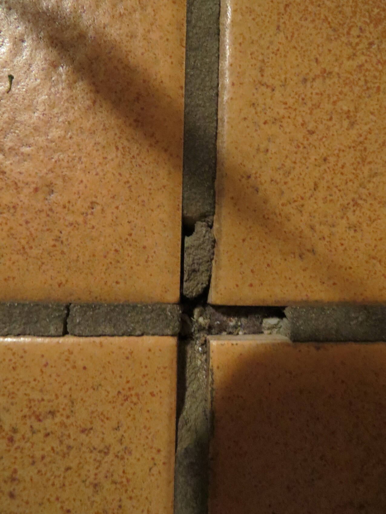 Close-up of damaged floor tiles with cracked grout and filler residue