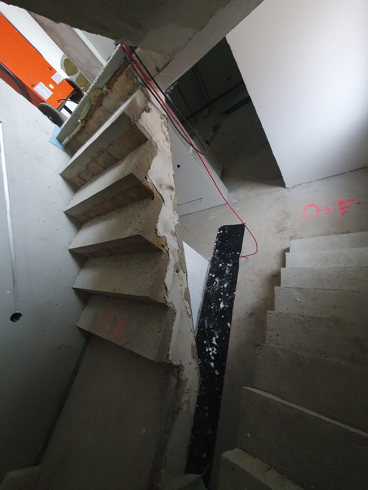 Construction site with raw concrete stairs, red cables, and orange construction equipment on the left side.