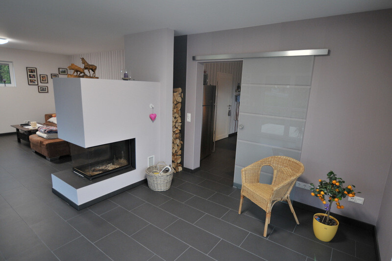 Modern living area with stove, wicker chair, plant, and glass sliding door to the kitchen.