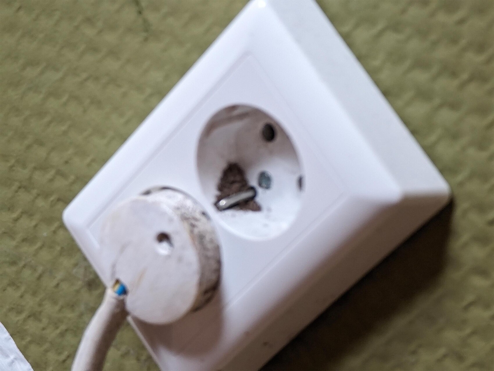 White double socket panel with dirty contacts; dust and a loose part nearby.