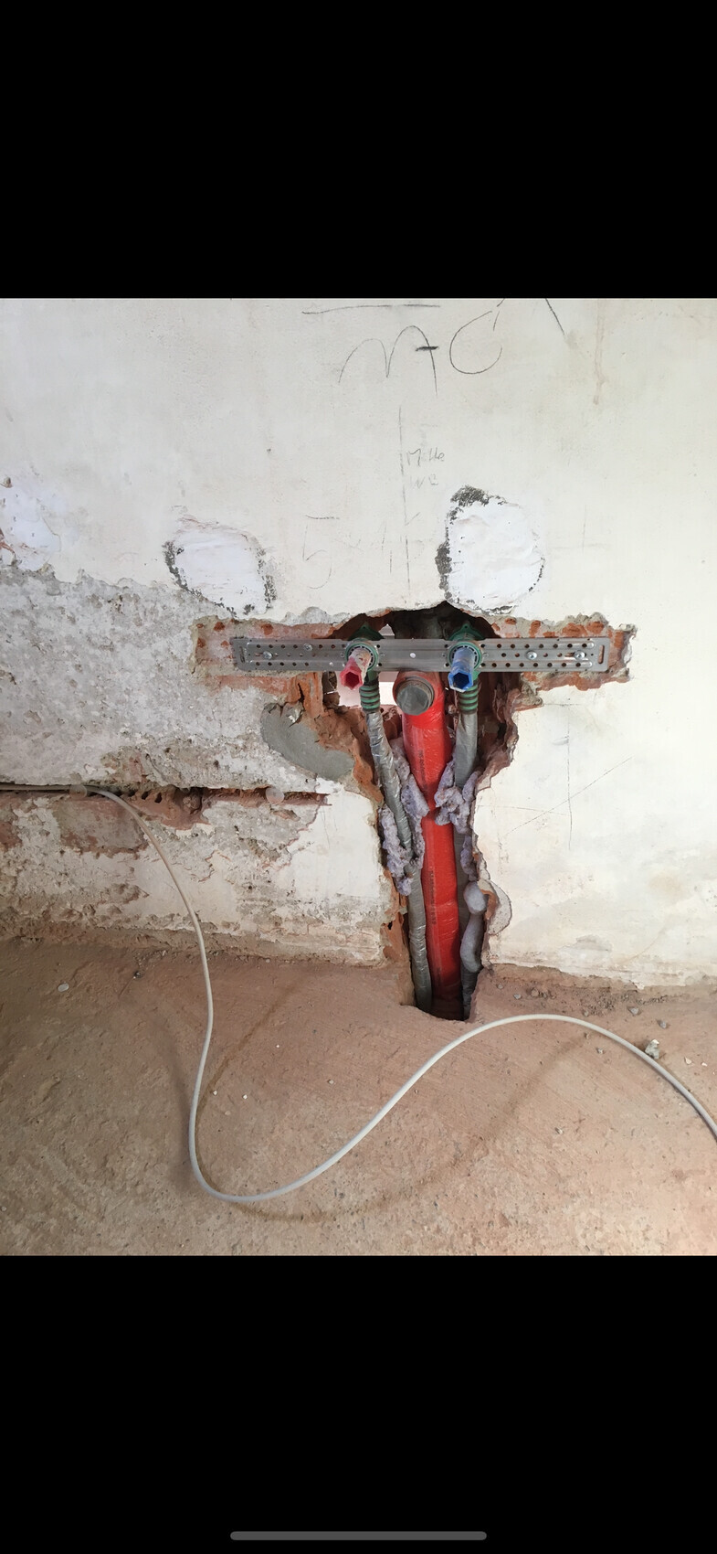 Open wall with red main pipe, two colored valves and metal bracket.