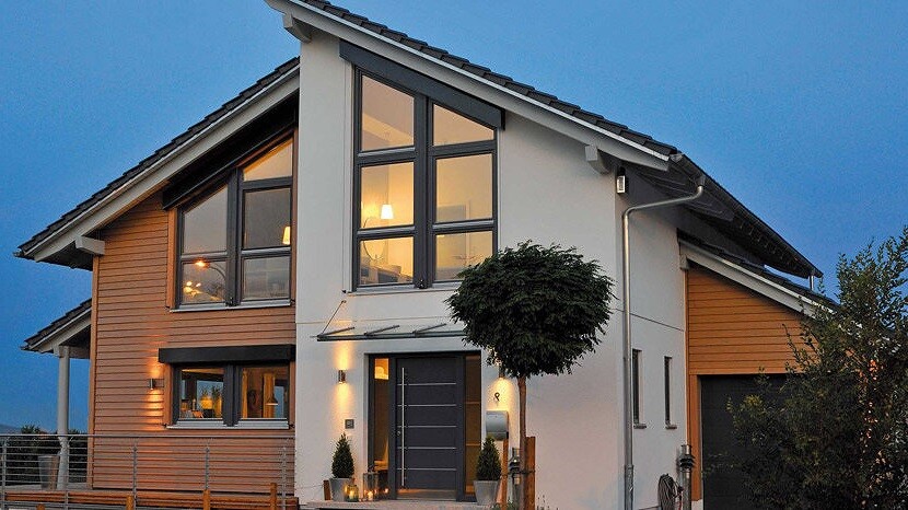 Modern two-story house with large windows, wood cladding, and evening lighting.