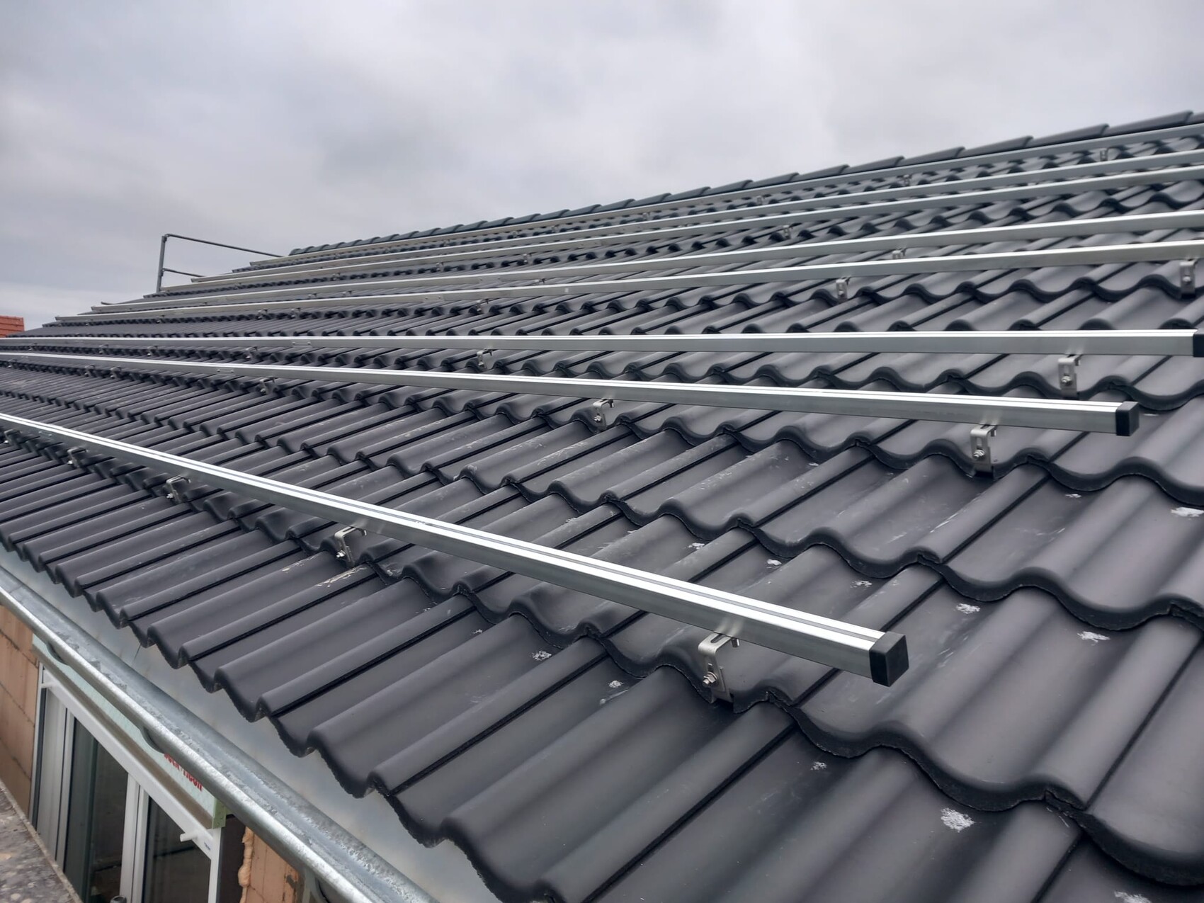 Roof with gray, wavy tiles and silver mounting rails for solar modules