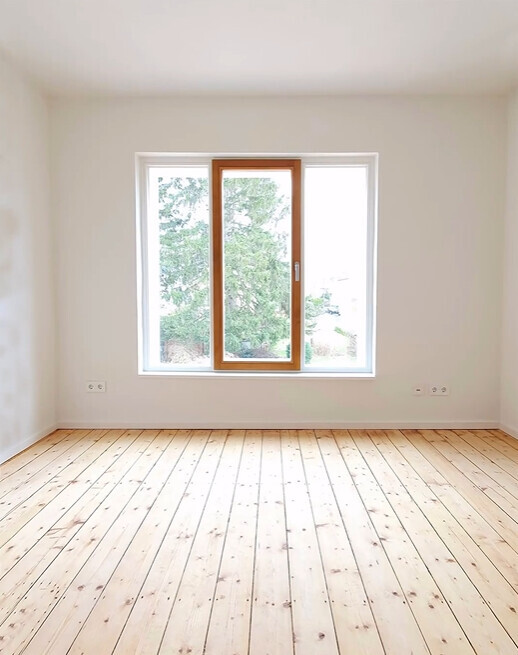 Bright empty room with wood parquet floor and large window with tree view.