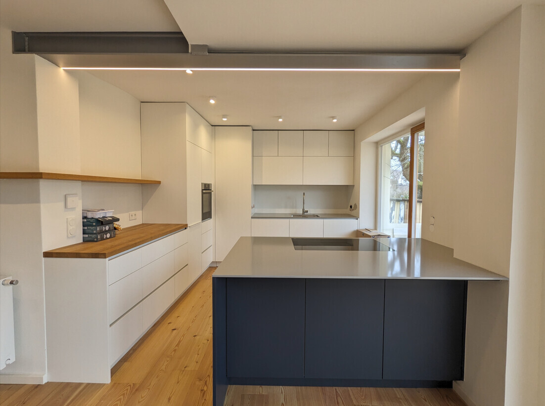 Modern kitchen with white cabinets, wooden countertop, dark kitchen island, and large window front