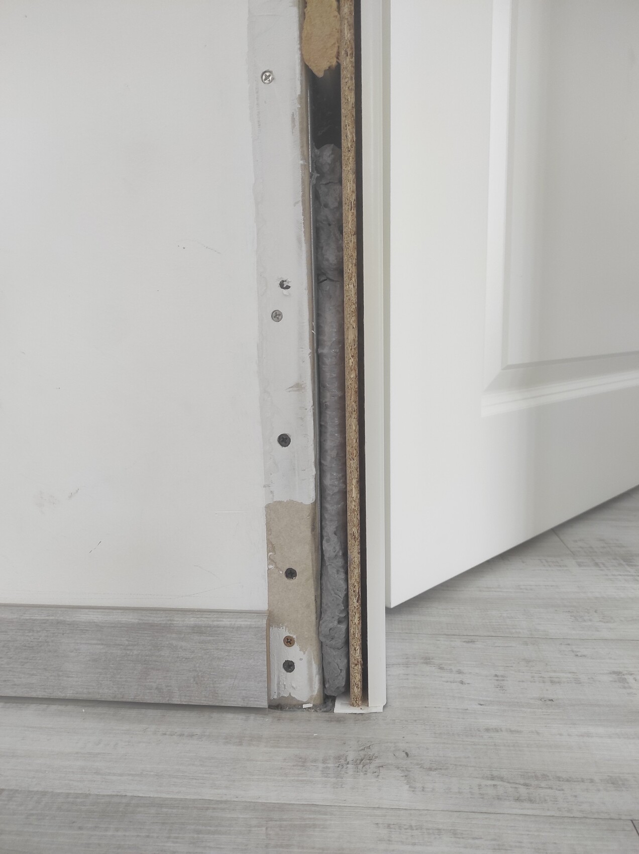 Door passage in renovation condition: open gap, insulation material and laminate floor visible.