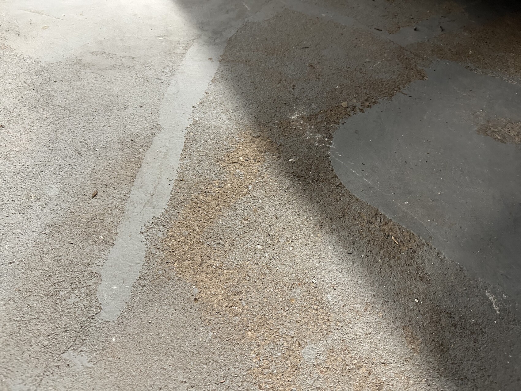 Asphalt floor with a dark, circular area on the right; sand lies along the edge next to it.