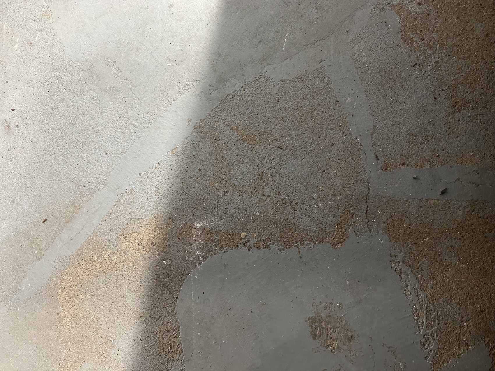 Close-up of a concrete floor with gray spots, brown rust stains, and shadows.
