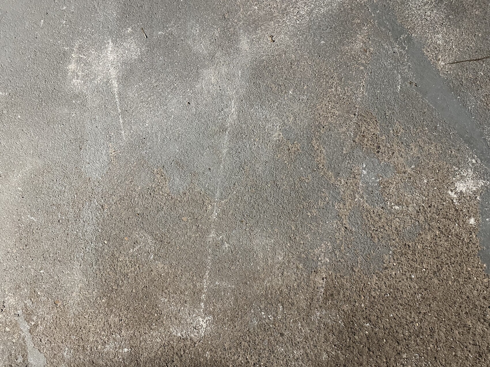 Concrete floor with gray spots, dust, and brown rust stains, coarse textured surface.