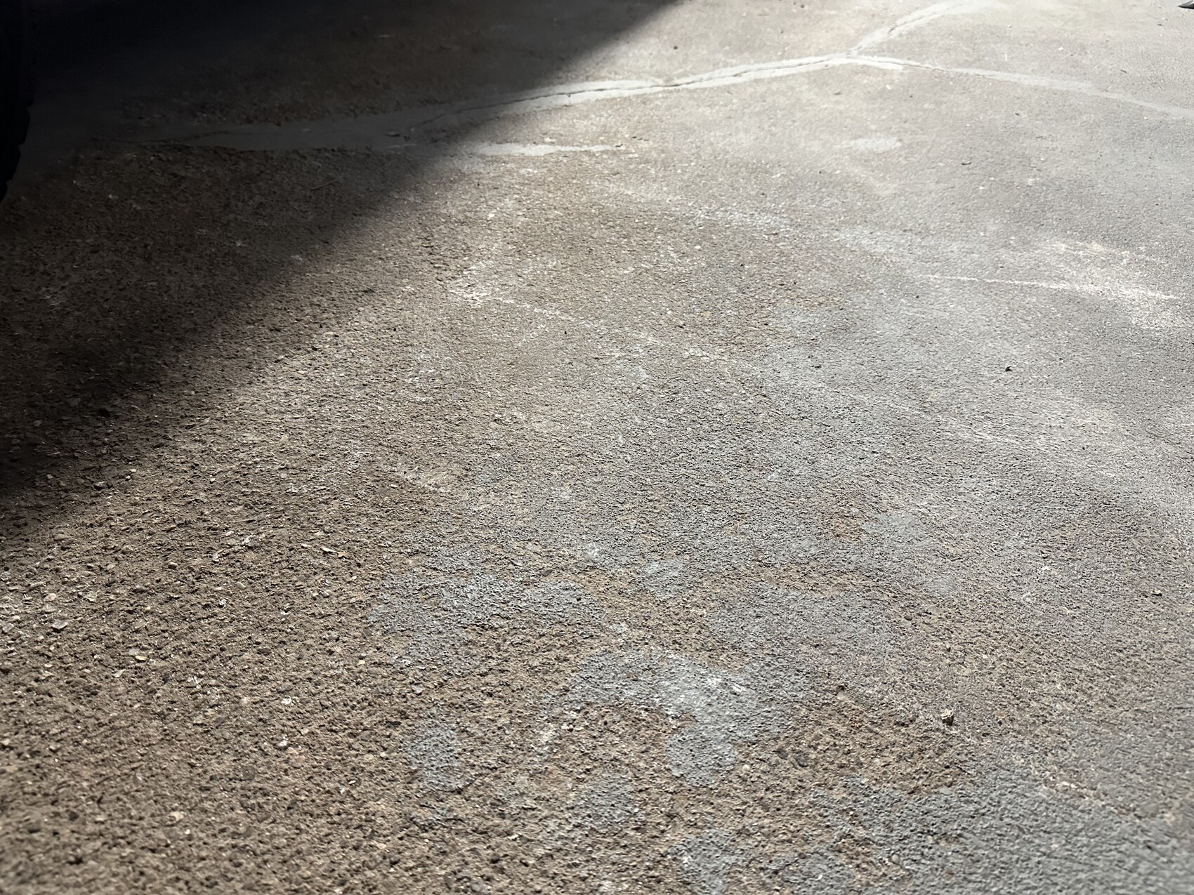 Asphalt surface with small gravel; the left area is in shadow, no people visible.